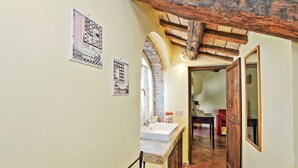 A narrow hallway with a sink and mirror on the left, a wooden door on the right, and a dining area in the background. - Volpe (Rome)