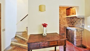 A wooden table with a vase of red flowers, a wall-mounted light, and a brick wall with a tiled backsplash. - Volpe (Rome)