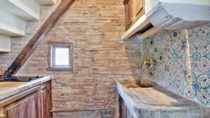 A rustic kitchen with exposed brick walls, wooden cabinets, a stone sink, and a tiled backsplash. - Volpe (Rome)