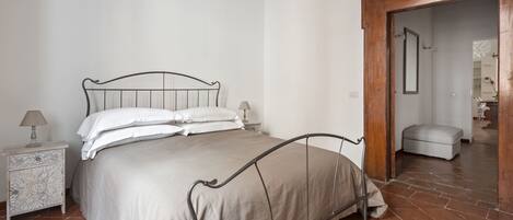 A bedroom with a bed, nightstand, and a wooden door leading to another room.