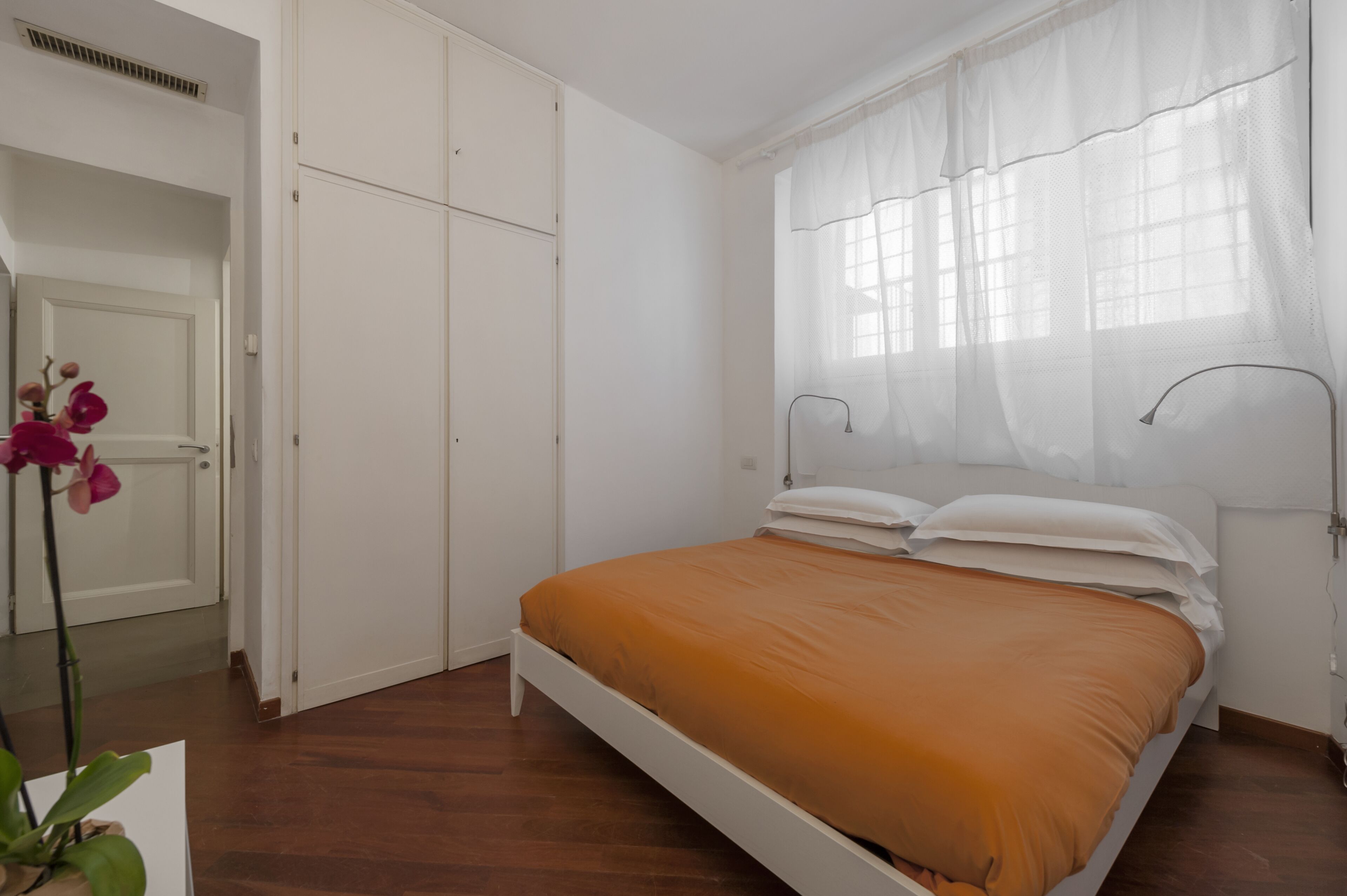 Une chambre à coucher avec un lit, une armoire blanche et une fenêtre ornée de rideaux légers.