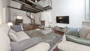 A modern living room with a glass coffee table, beige sofas, a staircase, and a flat-screen TV. - Volpe grande (Rome)
