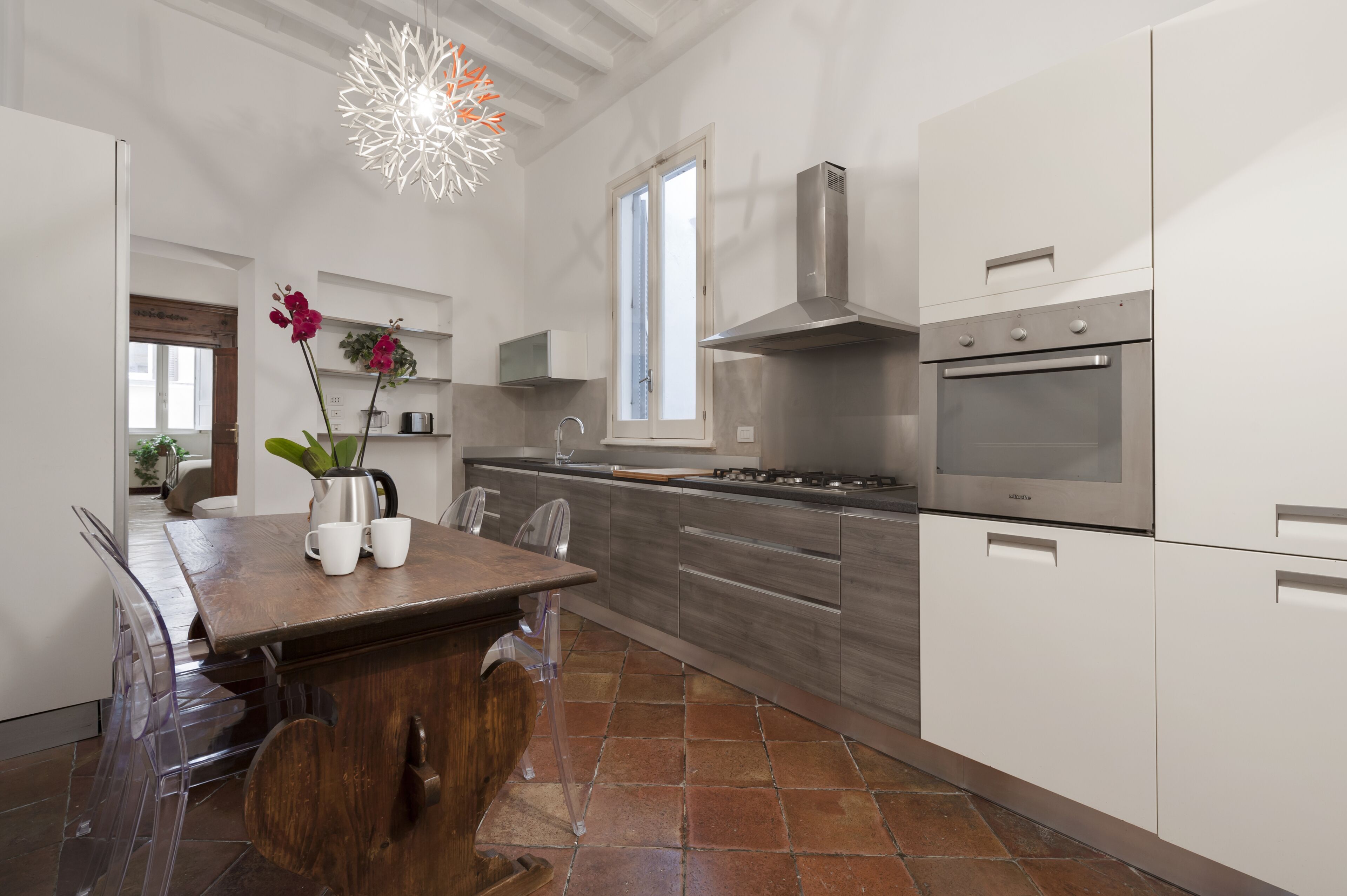 A modern kitchen with stainless steel appliances, a wooden dining table, and a clear glass chair.