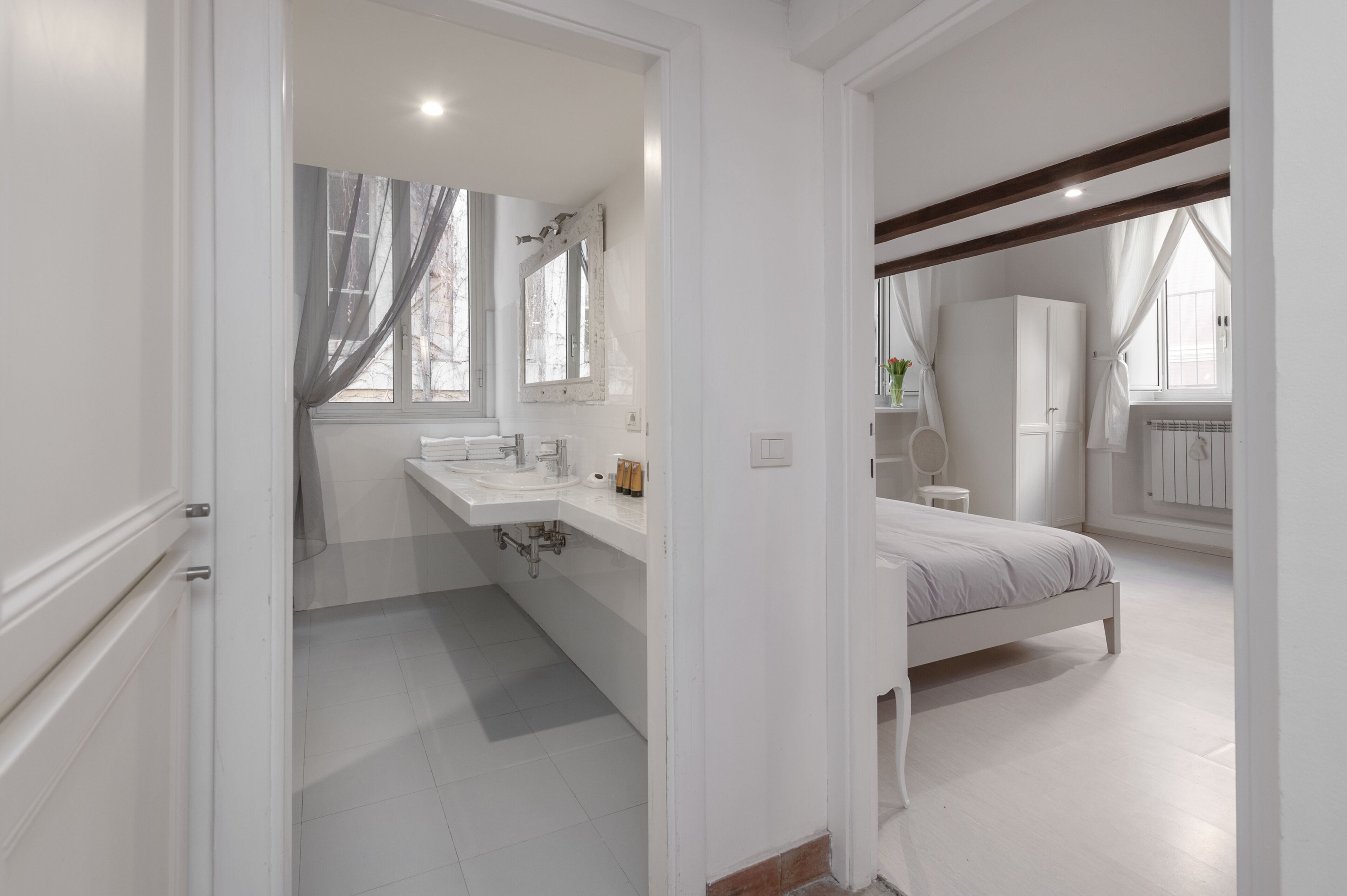 A bedroom with a bed, a large window, and a bathroom with a sink and mirror.