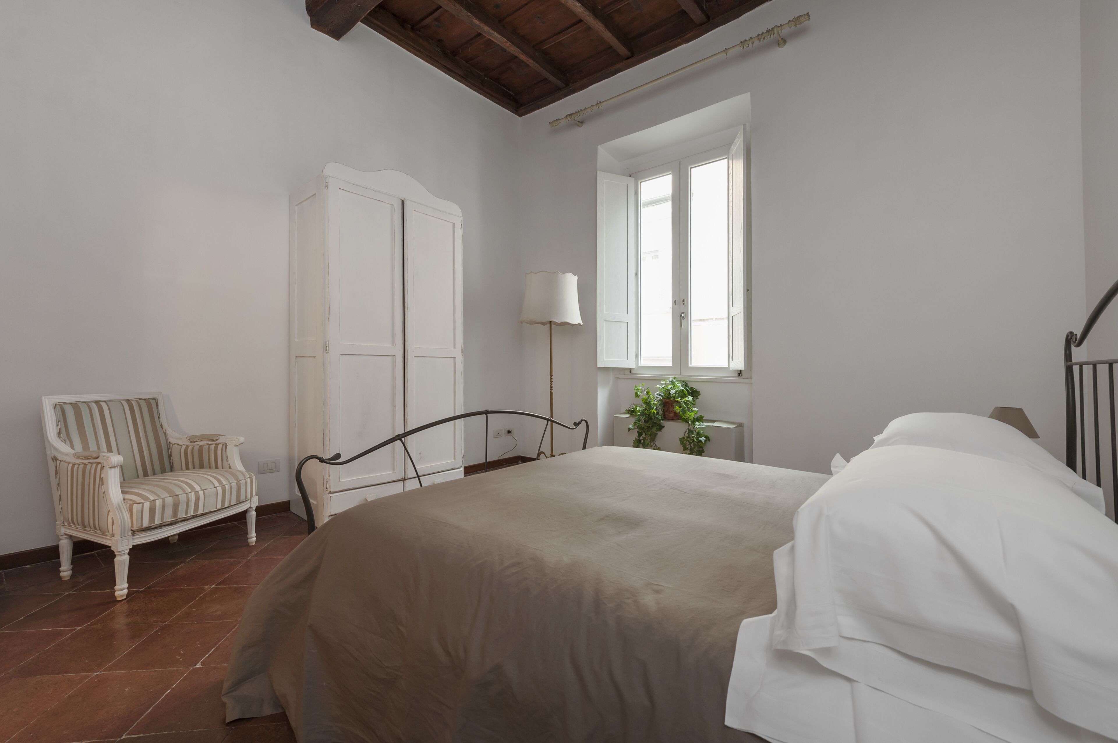 A bedroom with a bed, a chair, a wardrobe, a window, and a floor lamp.