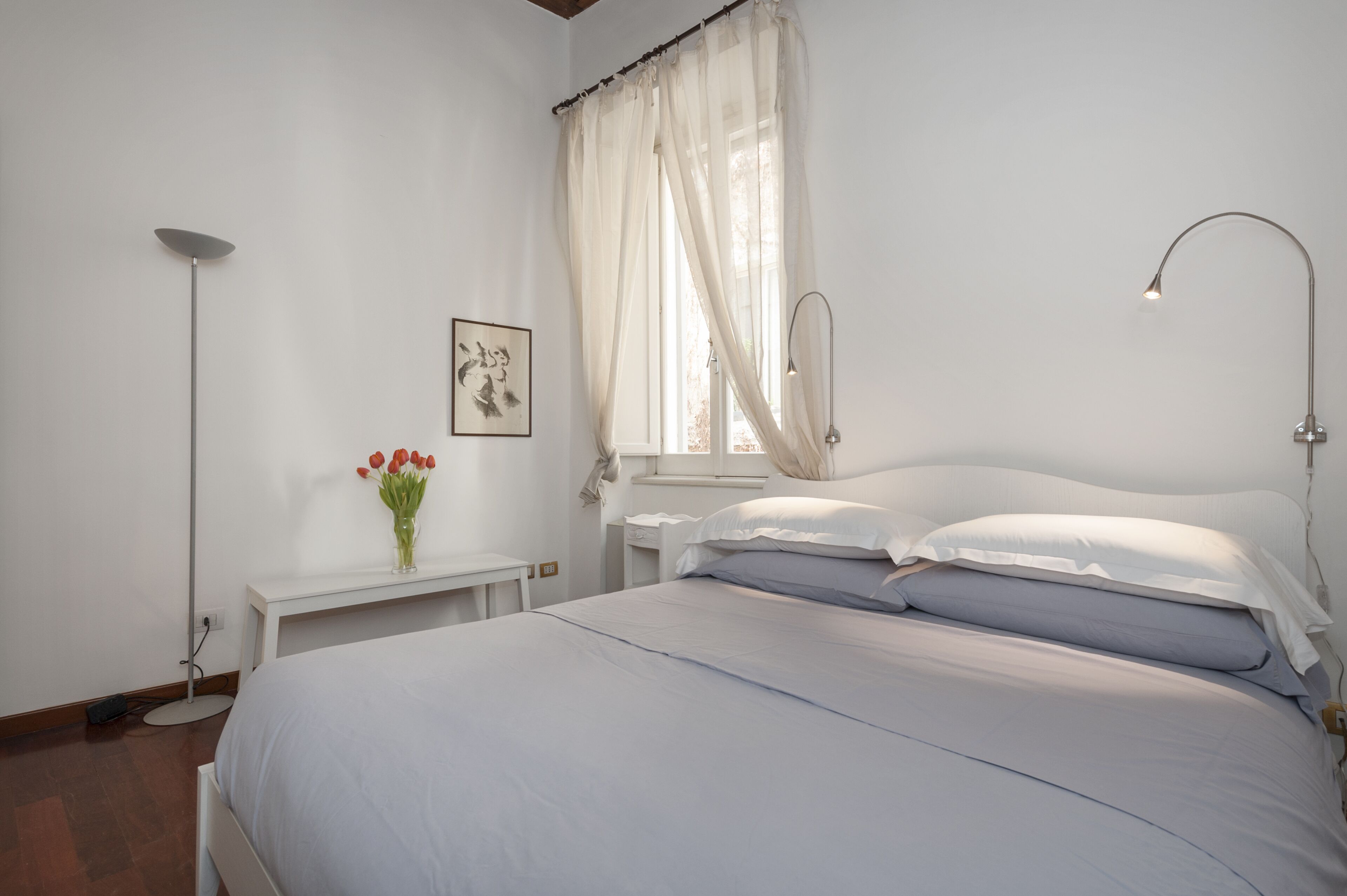 Une chambre à coucher avec un lit, une table de chevet, une lampe et une fenêtre avec des rideaux.