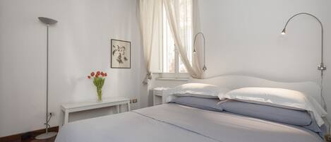 Une chambre à coucher avec un lit, une table de chevet, une lampe et une fenêtre avec des rideaux.
