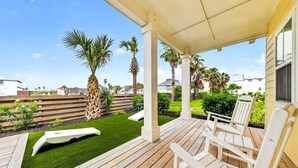 Un espacio al aire libre cubierto con un suelo de madera, sillas reclinables blancas y un césped artificial pequeño.