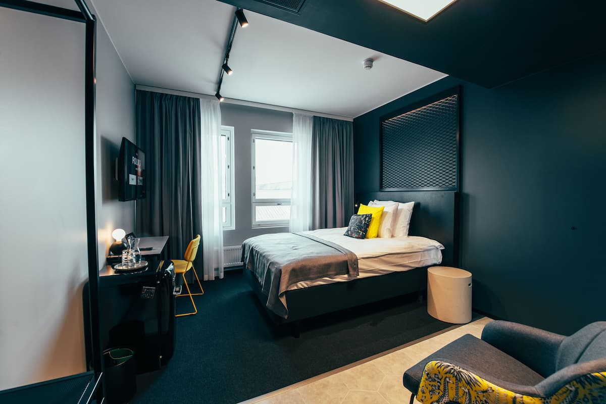 Una habitación de hotel moderna con cama, escritorio, silla y una mesita.