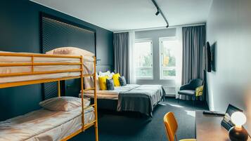 A hotel room with a bunk bed, a single bed, a desk with a lamp, a chair, and a TV.