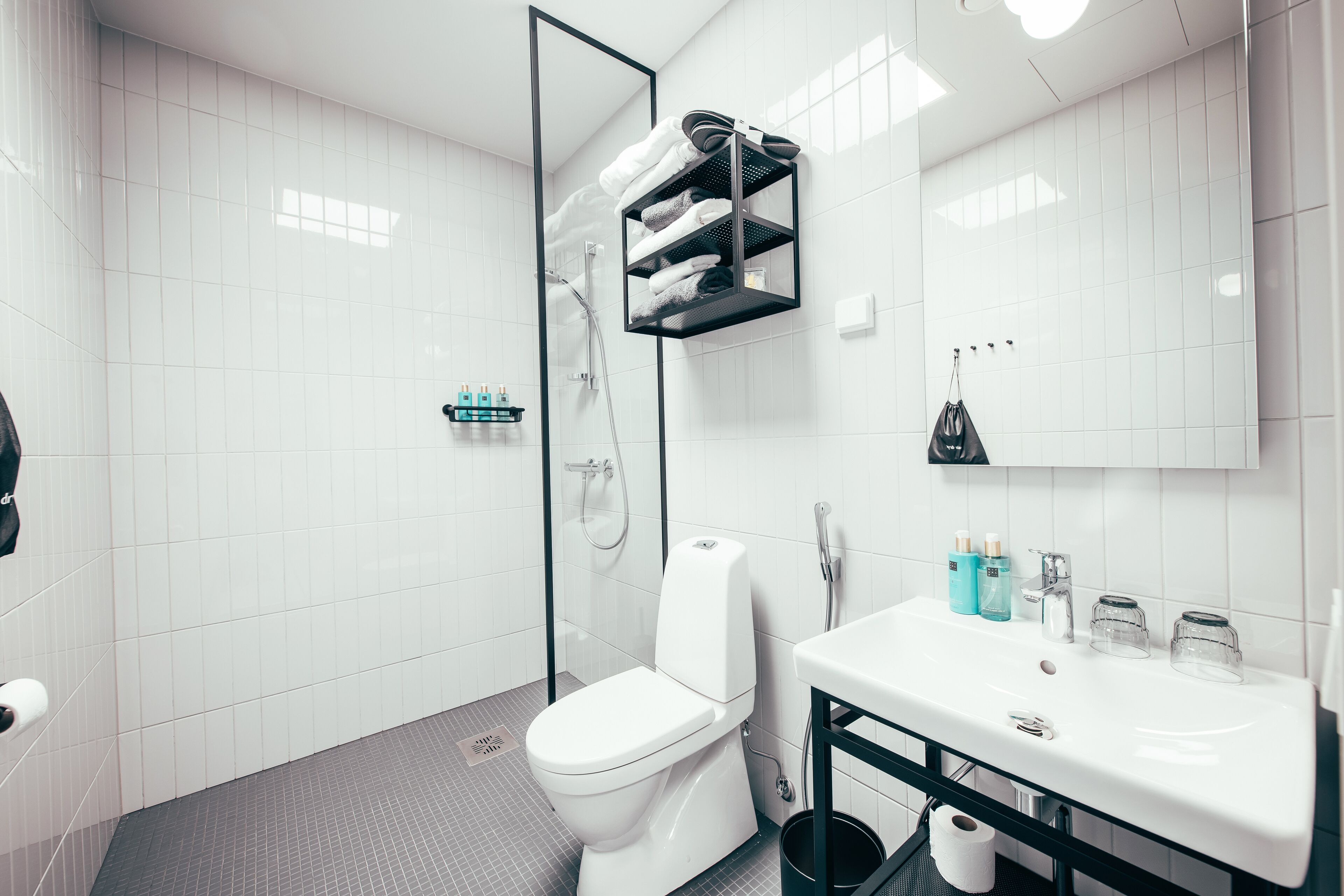 Un baño moderno con inodoro blanco, cabina de ducha de cristal, lavabo blanco con mueble negro y espejo sobre el lavabo.