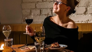 Una persona sentada a una mesa redonda con una vela, copas de vino y platos de comida.