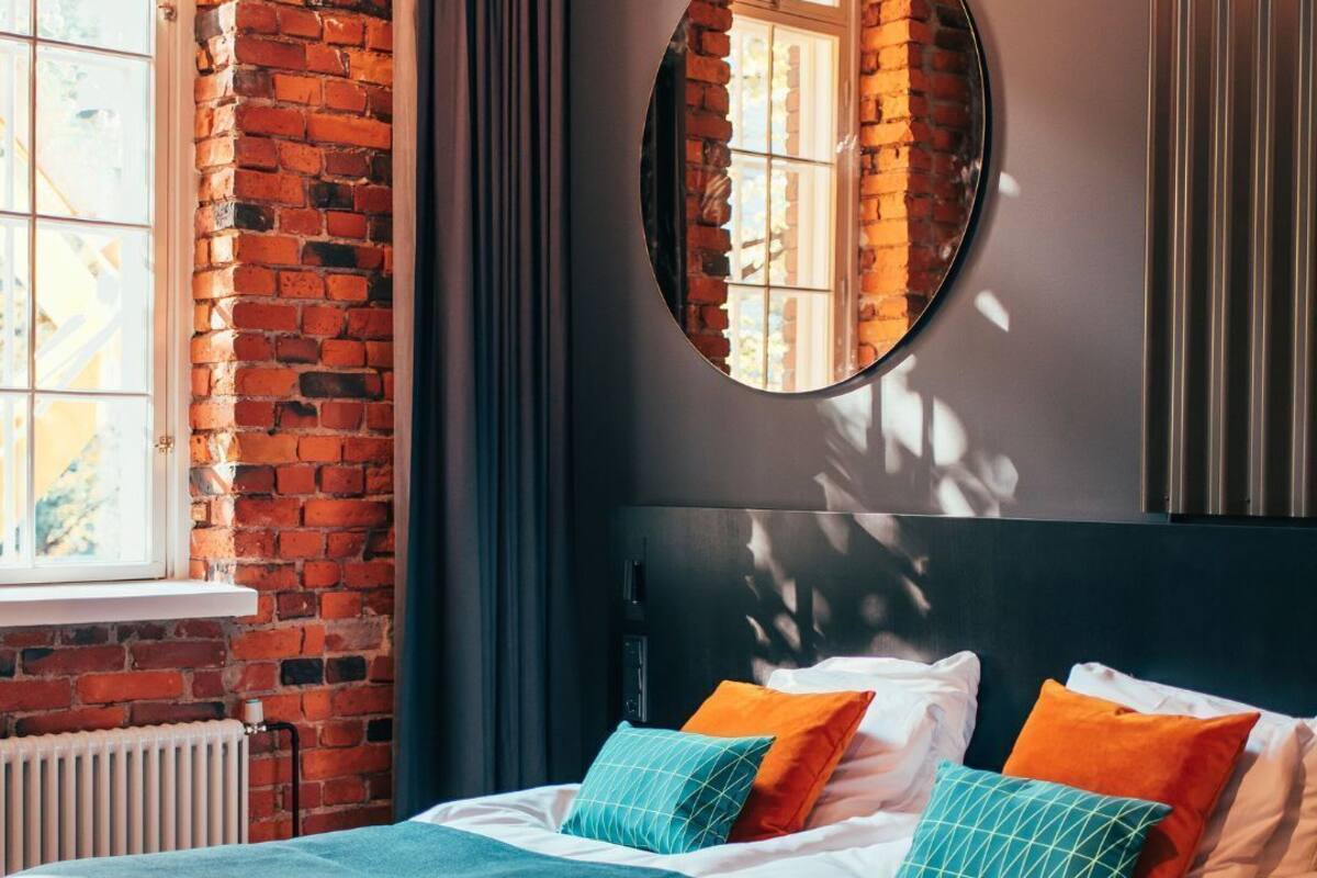 Una cama con cabecera, un espejo redondo y una ventana con cortinas.