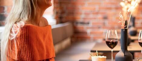 Une personne assise à une table, devant une bougie, un verre de vin et des plats.