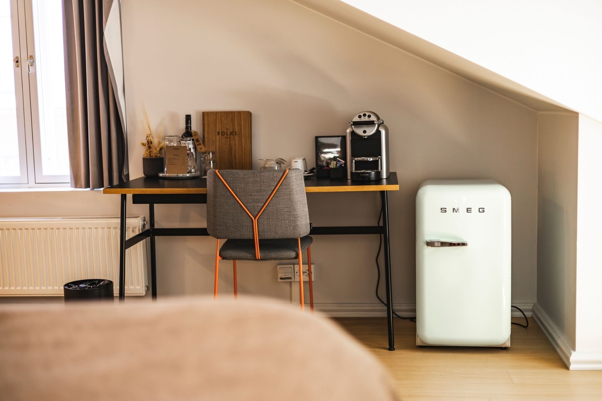 A modern kitchenette with a white refrigerator, a coffee machine, and a chair with orange accents.