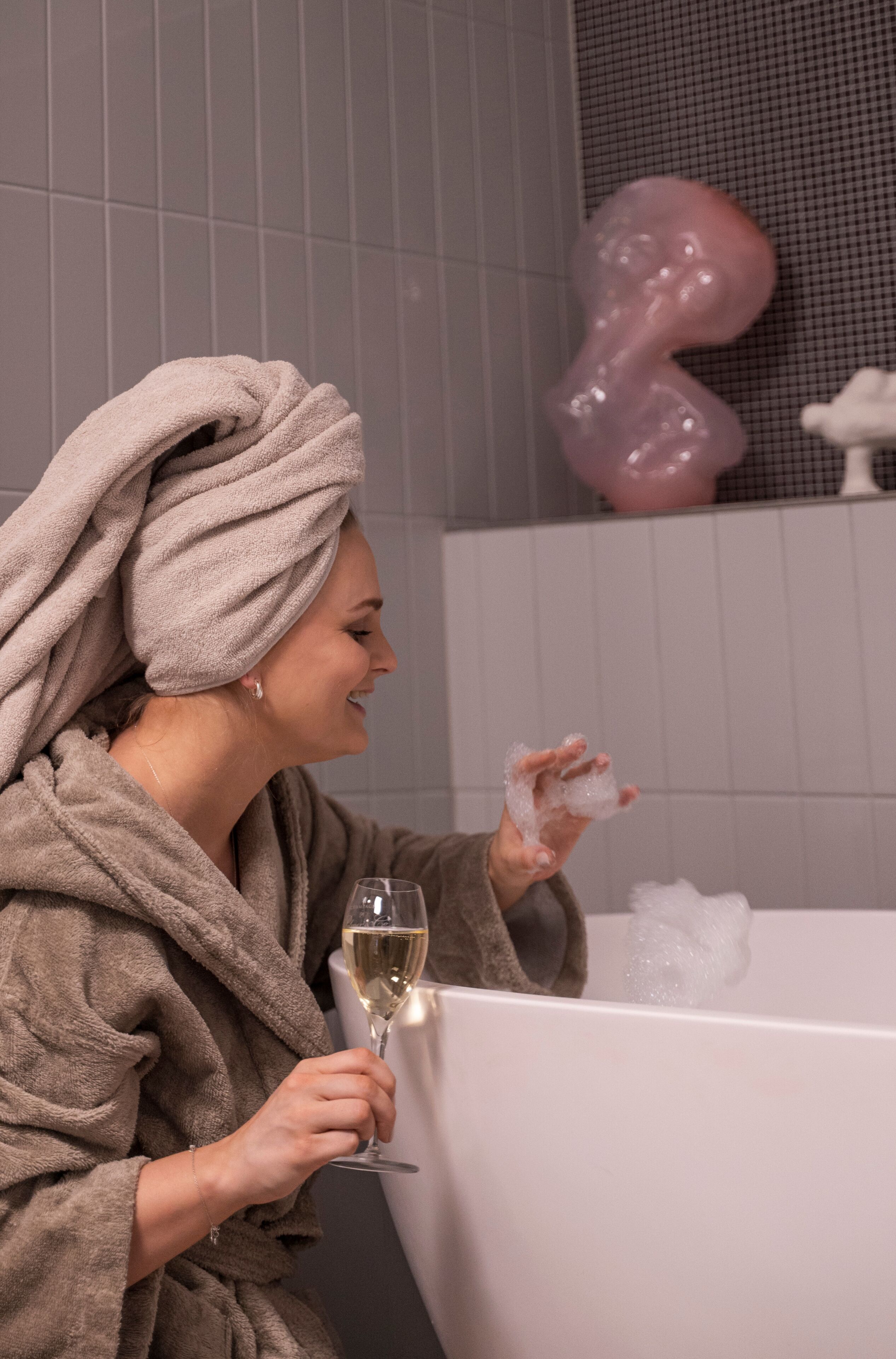 Iemand in een badjas die een glas witte wijn vasthoudt in een bad vol bubbels.