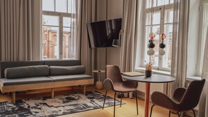 Una sala de estar moderna con un sofá, sillas, un televisor y vistas a edificios a través de amplios ventanales.