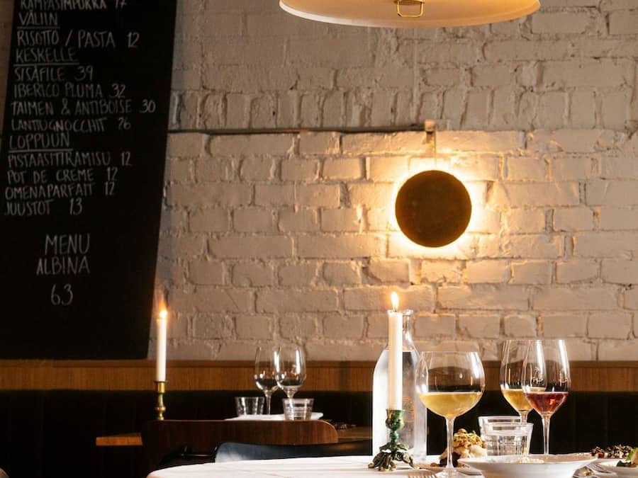 A restaurant interior with a brick wall, a hanging pendant light, a menu on the wall, and a table set for dining.