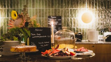 Un bufé de desayuno con gran variedad de alimentos, una cúpula de vidrio que cubre bebidas, y una vela.