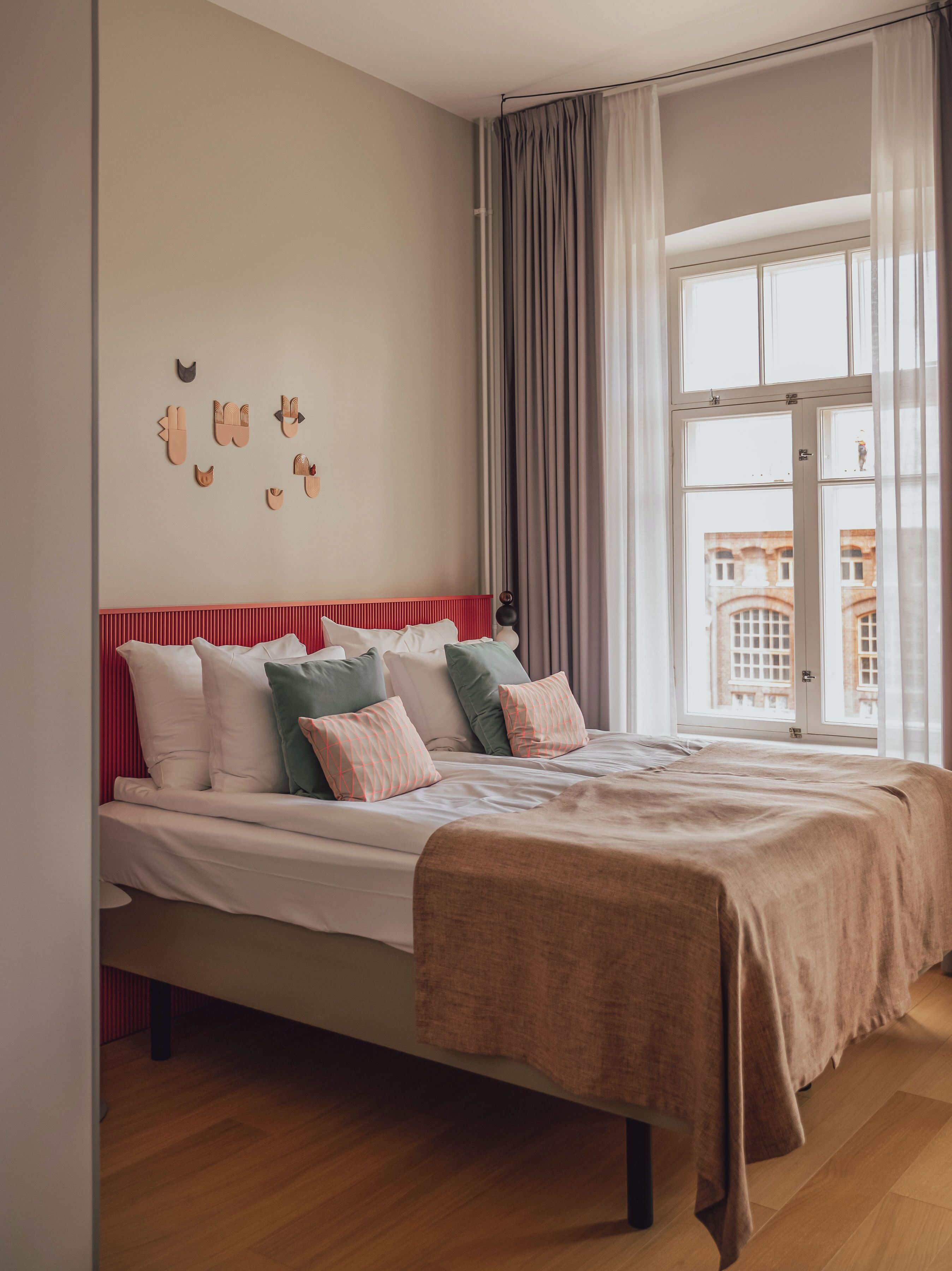 A bedroom with a bed, a window with curtains, and a view of buildings outside.