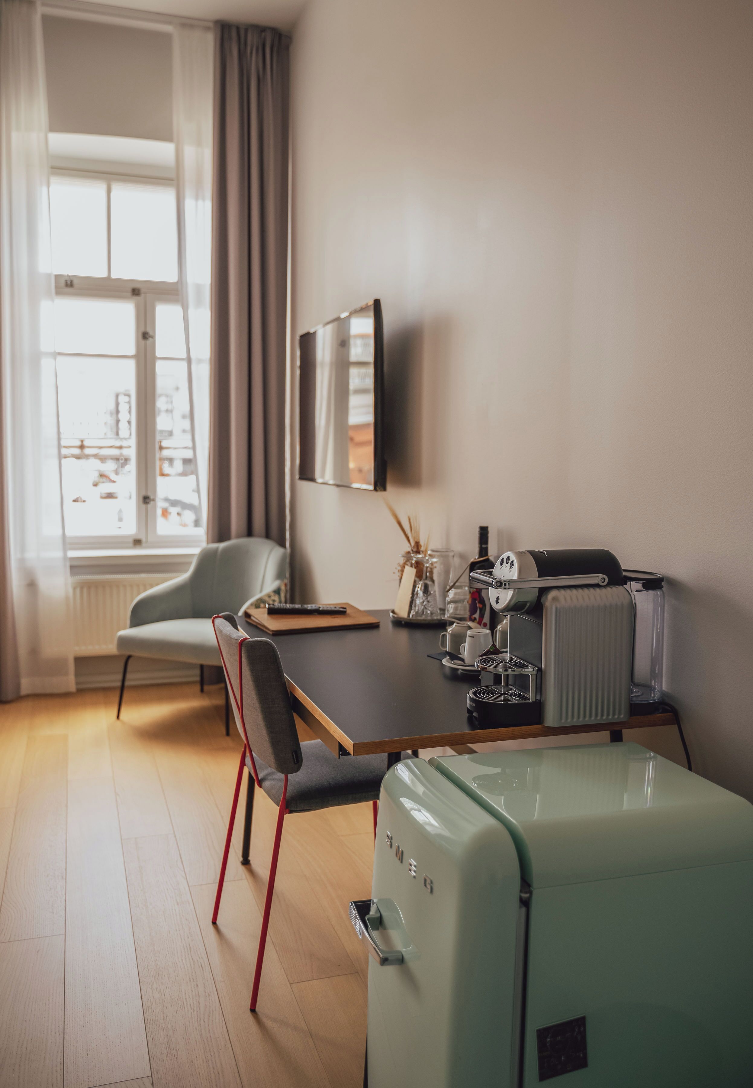 Um espaço compacto com mesa de jantar, uma cadeira, frigorífico estilo vintage, radiador e janela com cortinas.