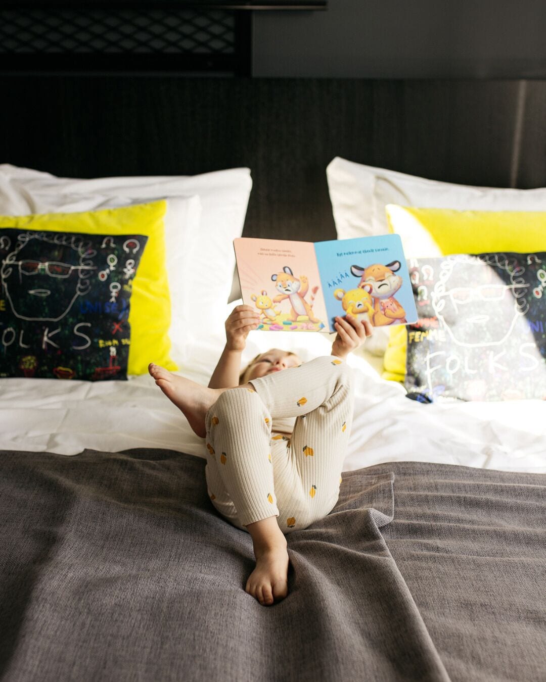 A child lying on a bed with pillows, reading a book.