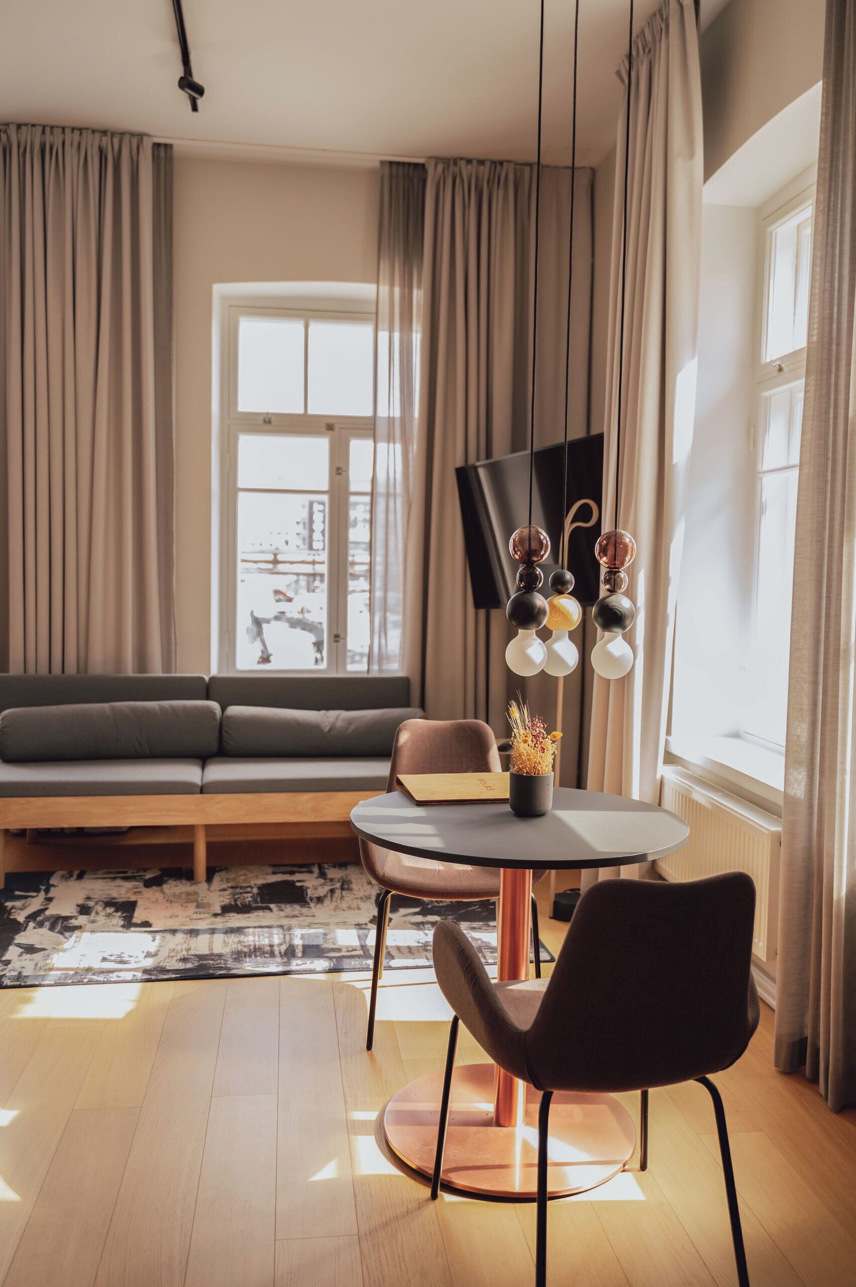 A modern living room with a sofa, a dining table with chairs, a flat-screen TV, and a window with curtains.