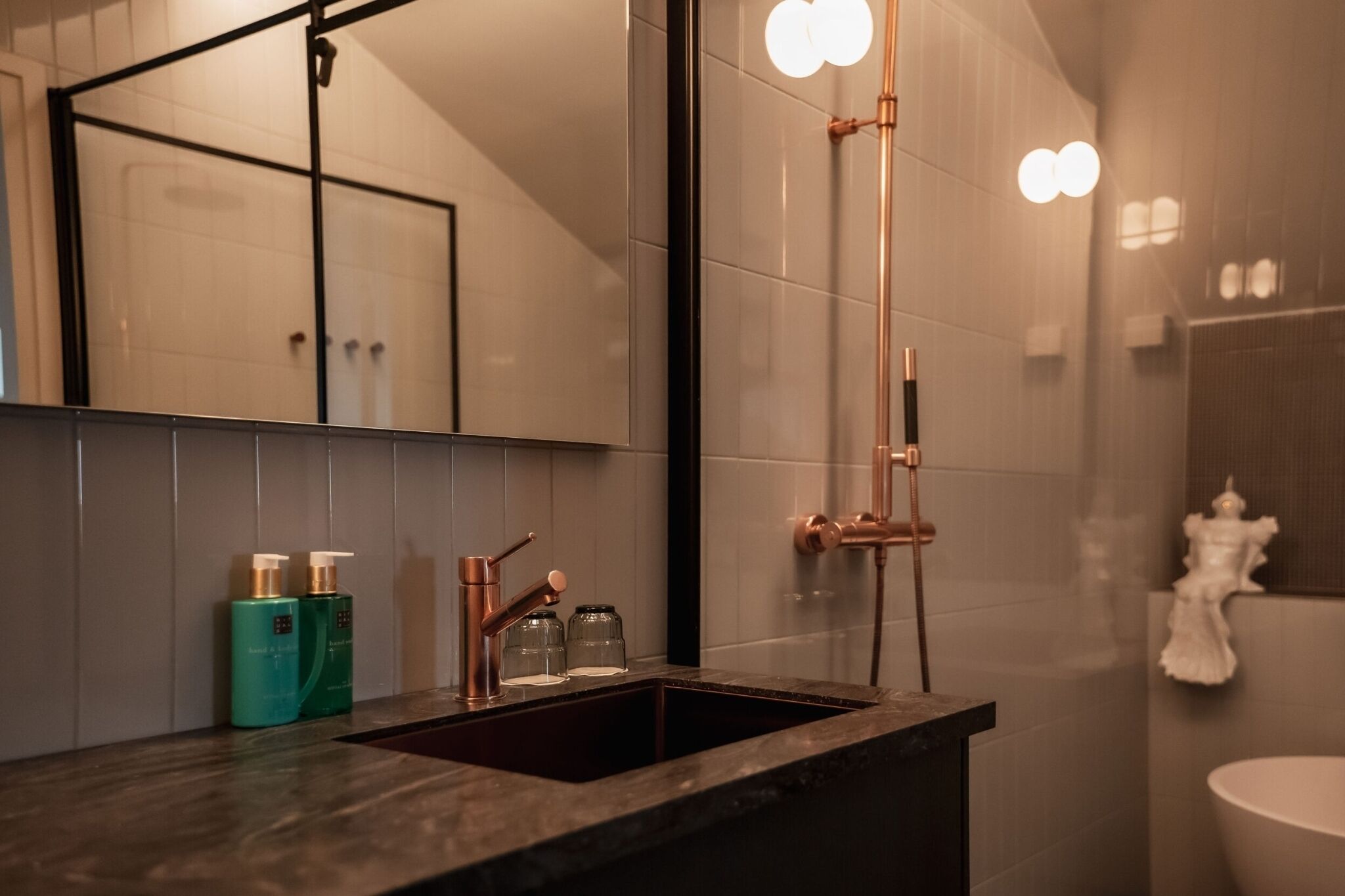 Ein Badezimmer mit dunkler Arbeitsplatte, Waschbecken, Spiegel und Dusche mit Glastrennwand.