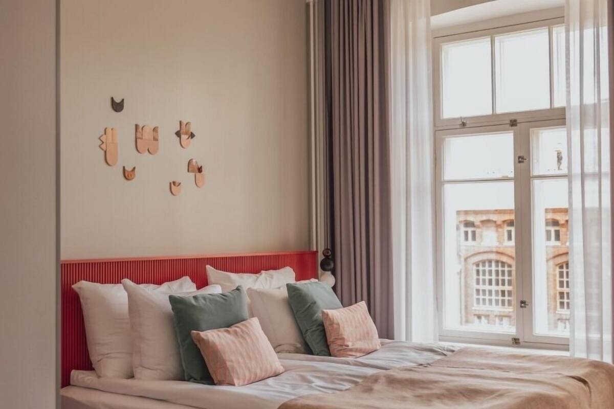 Un dormitorio con cama, almohadas, cabecera roja, ventana con cortinas y pared decorada con recortes de animales de madera.
