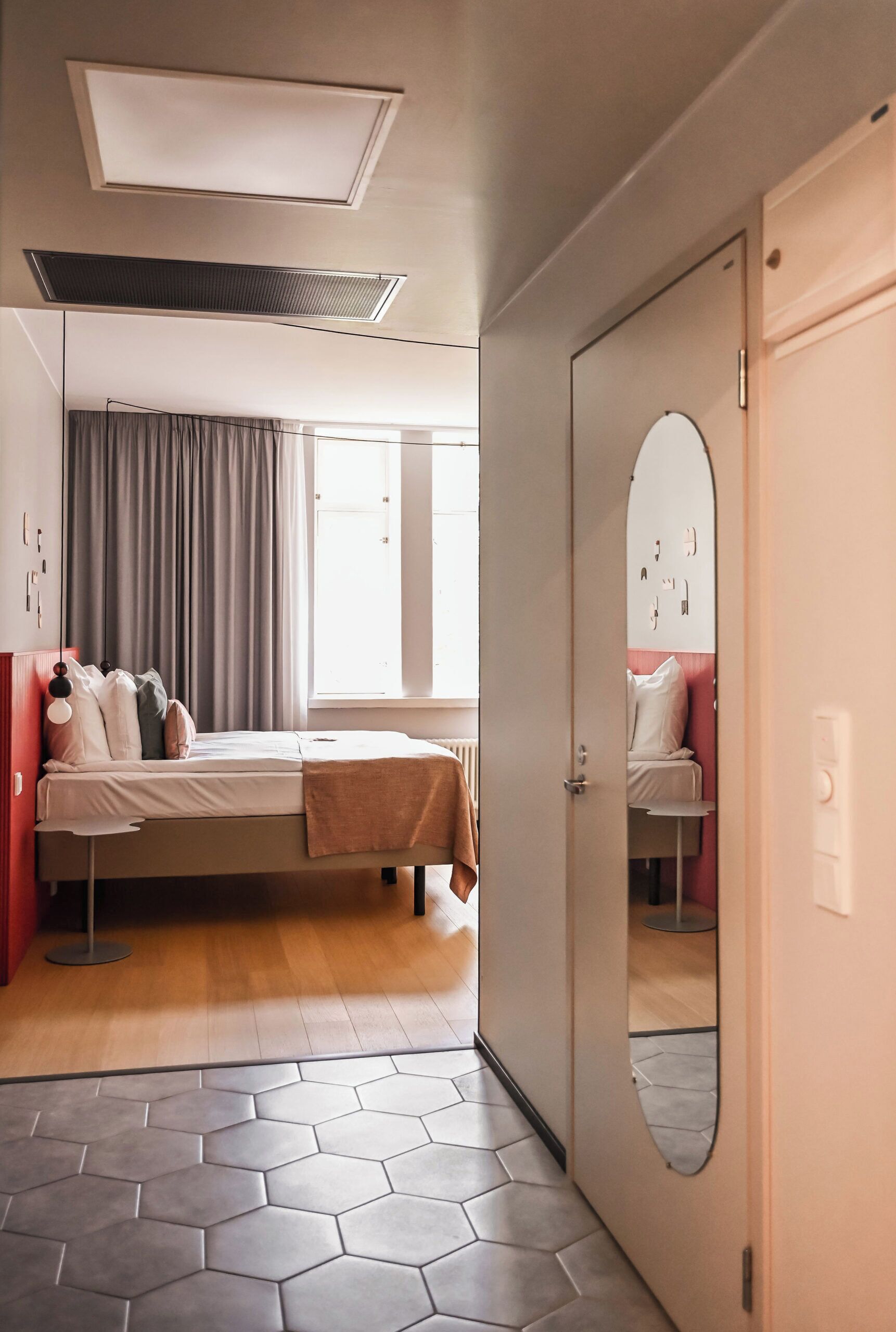 A hotel room with a bed, a mirror, a door, and a window.