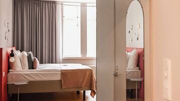A hotel room with a bed, a mirror, a door, and a window.