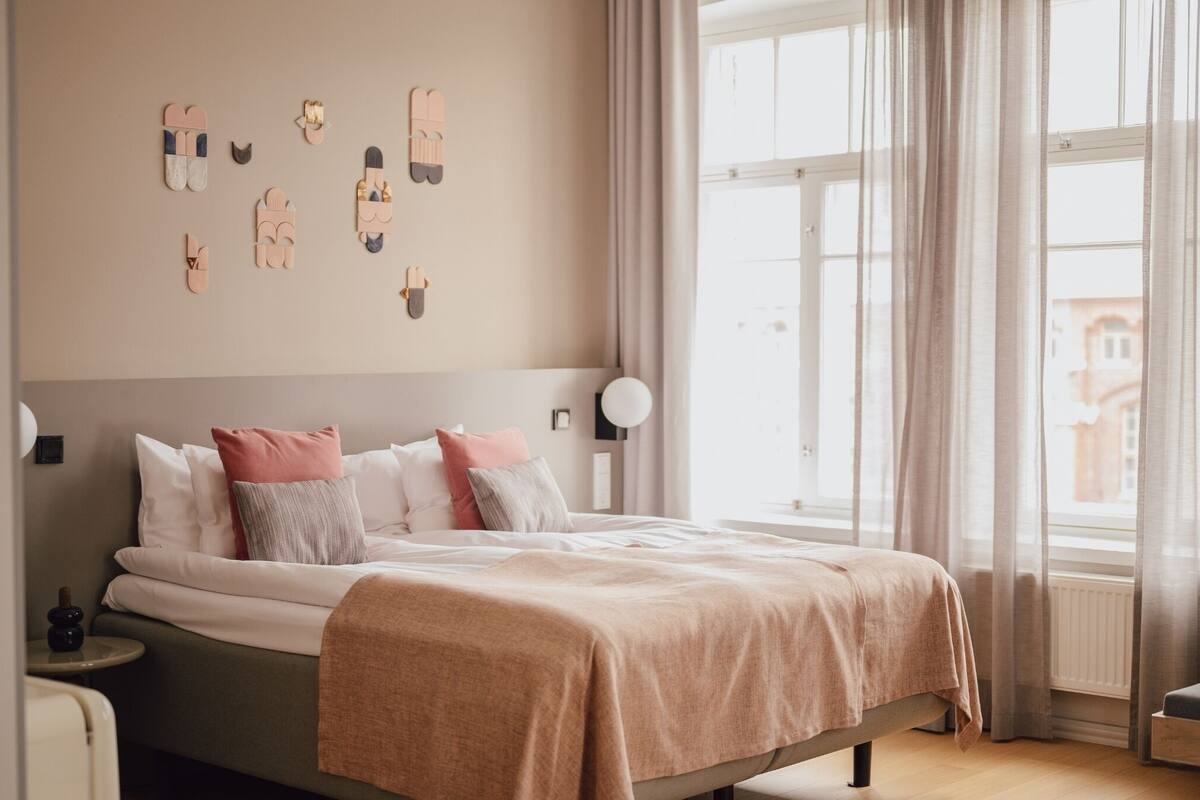 Un dormitorio con cama, mesita de noche, reloj en la pared y ventana con cortinas.