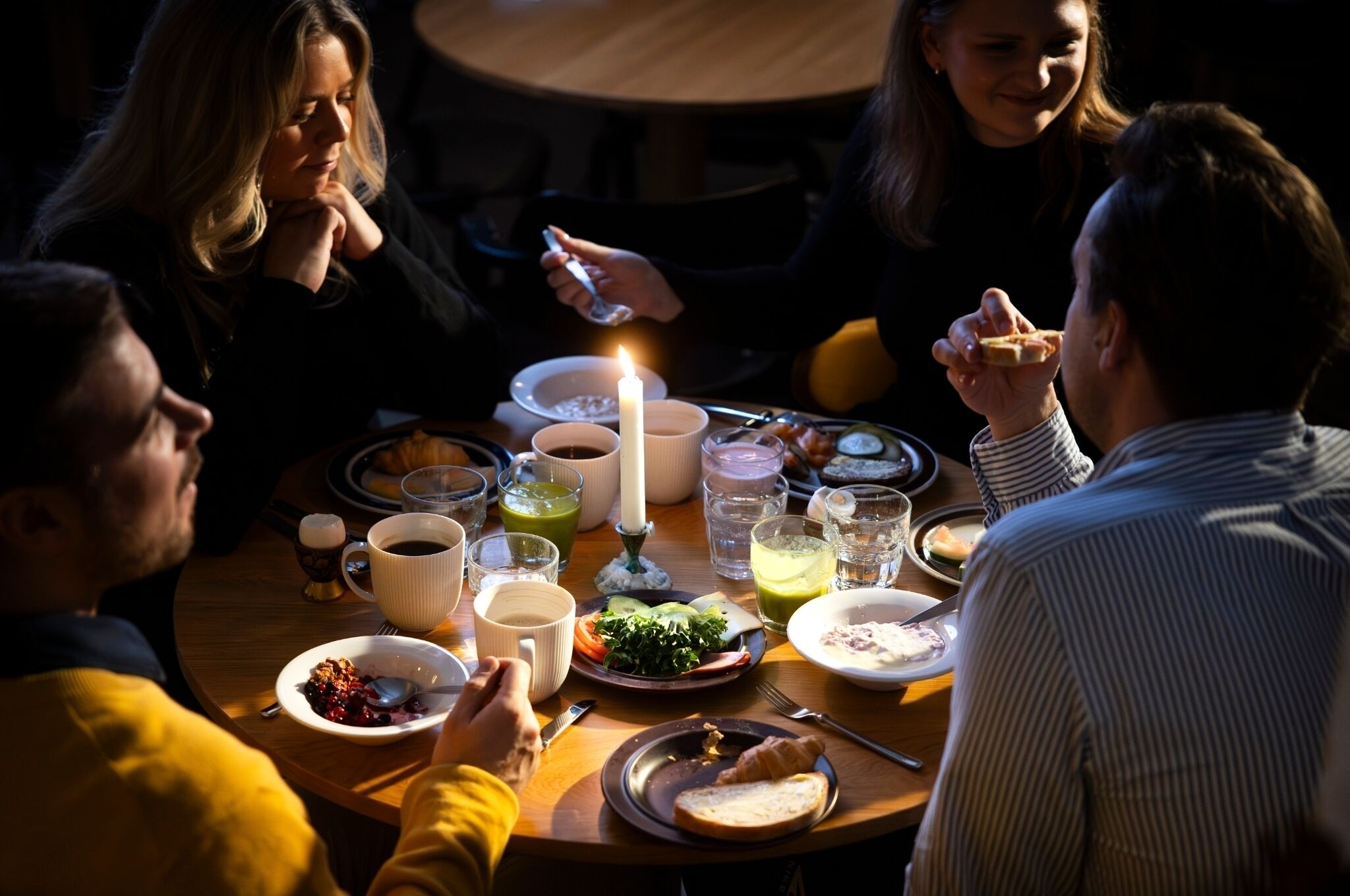 Uma mesa de jantar redonda com vários pratos, copos e uma vela acesa.