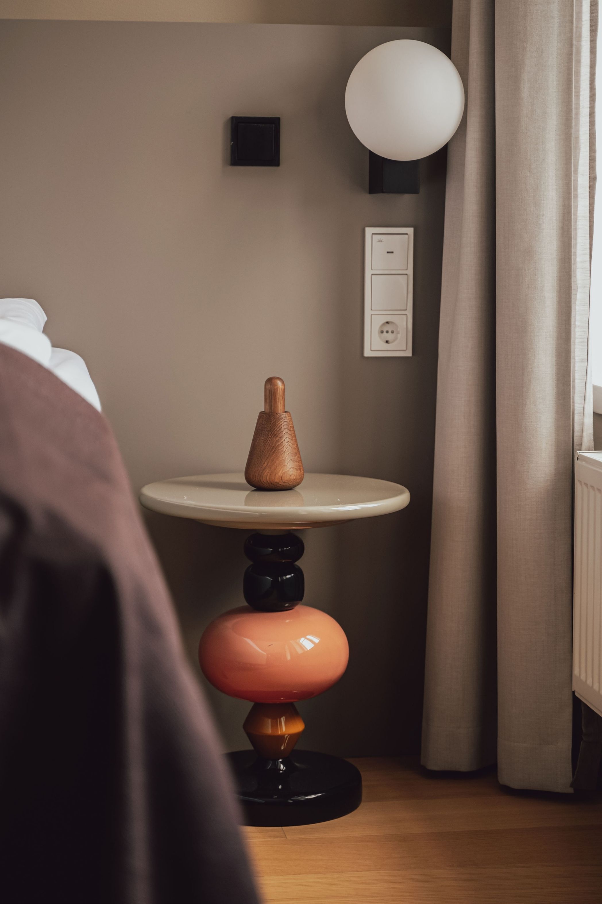 A room with a round table, a wall socket, a lamp, and a curtain.