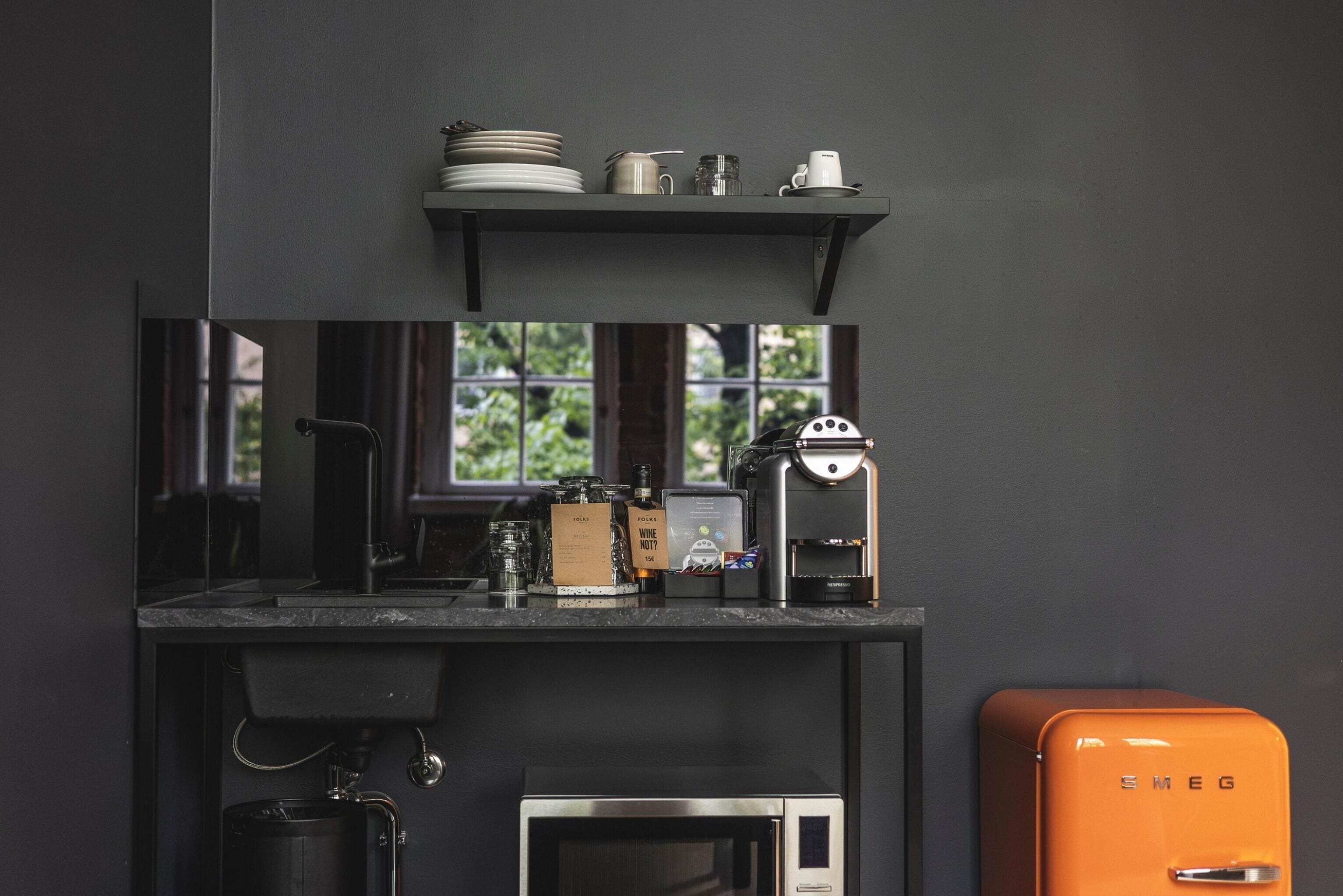 A kitchen with a coffee machine, microwave, and a vintage orange refrigerator.