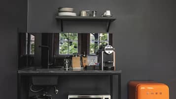 A kitchen with a coffee machine, microwave, and a vintage orange refrigerator.