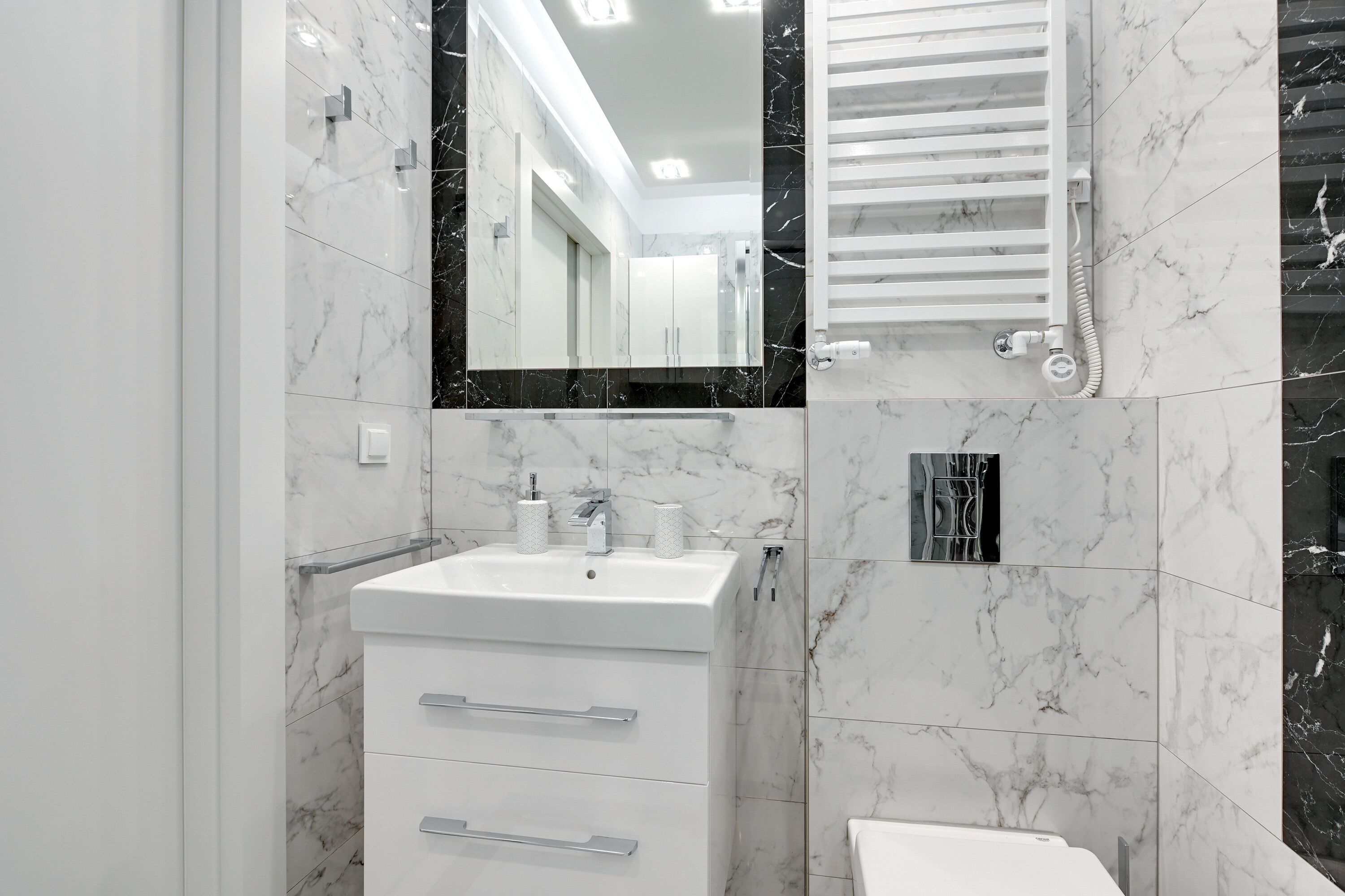 Une salle de bain moderne avec un lavabo blanc, des carreaux de marbre et un grand miroir.