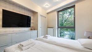 Ein modernes Schlafzimmer mit großem Fenster, einem flachbildfernseher an der Wand und einem ordentlich bezogenen Bett.