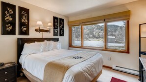 Ein ordentlich eingerichtetes Schlafzimmer mit einem großen Bett, Nachttischlampen und Kunstwerken an den Wänden.