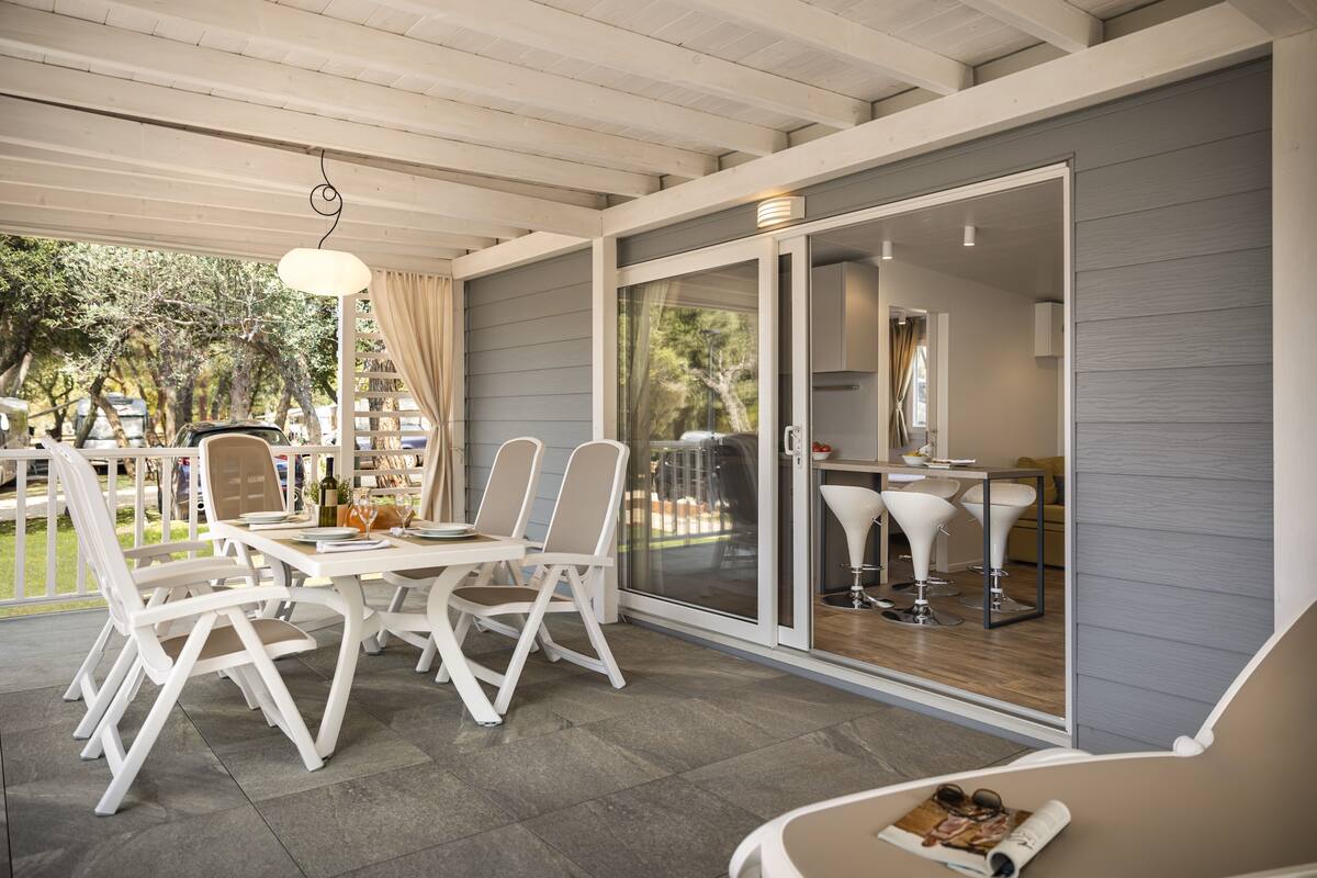 A covered patio area with a dining table and chairs, a sofa, and a sliding glass door leading to a kitchen.