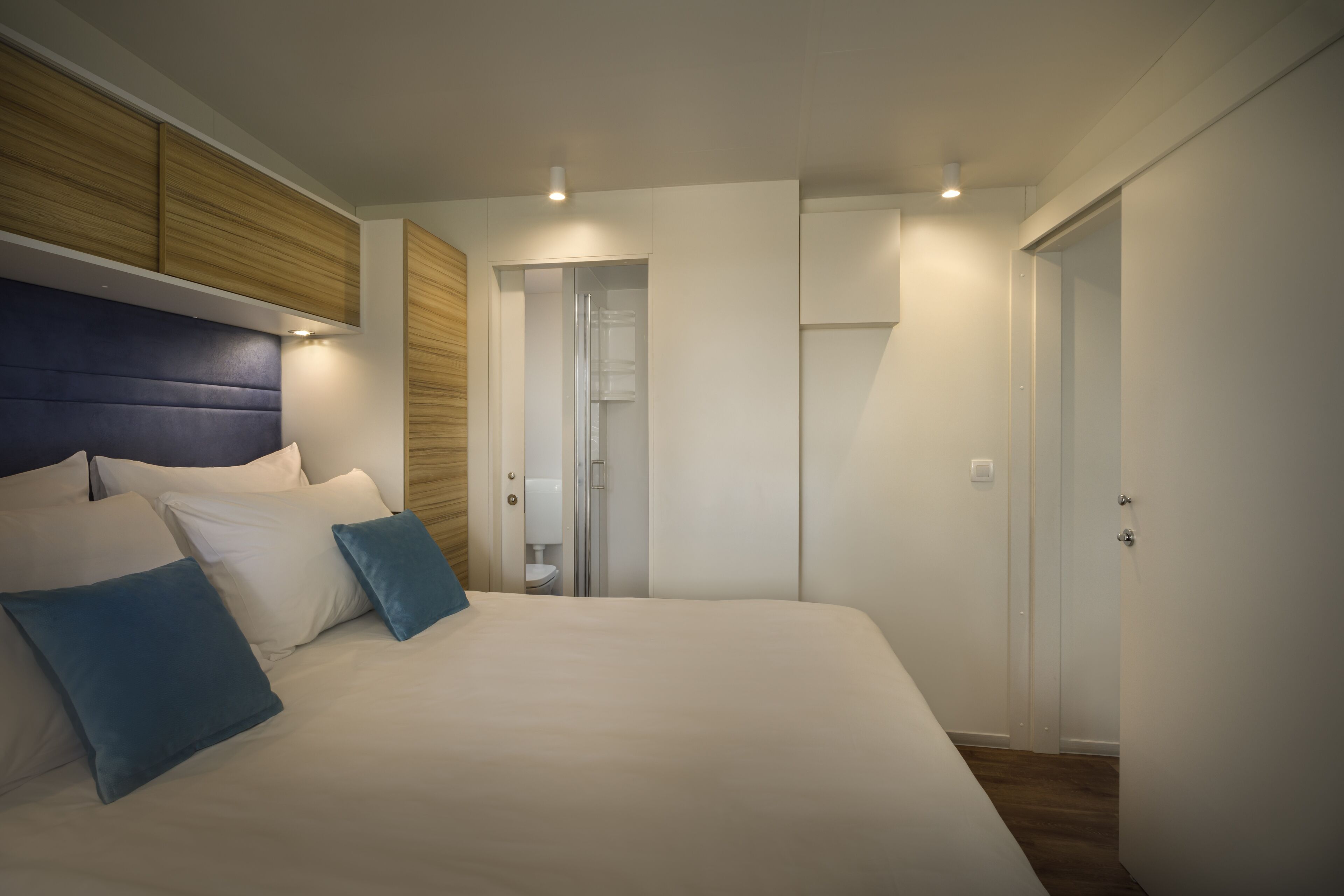 A modern bedroom with a large bed, built-in wooden headboard, and a walk-in closet.