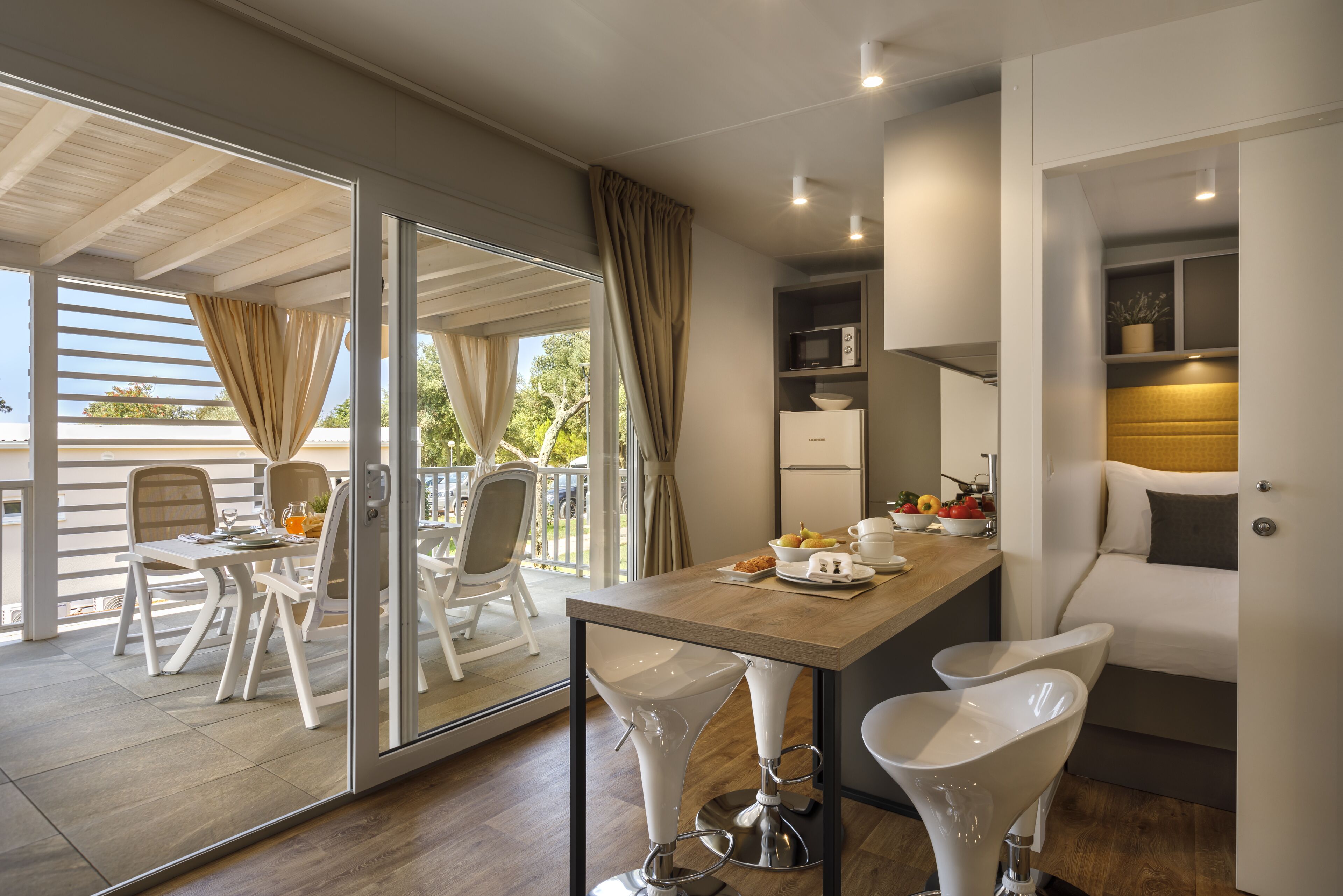Cozinha moderna com bancada de madeira, banquetas brancas e uma área de refeições com mesa e cadeiras.