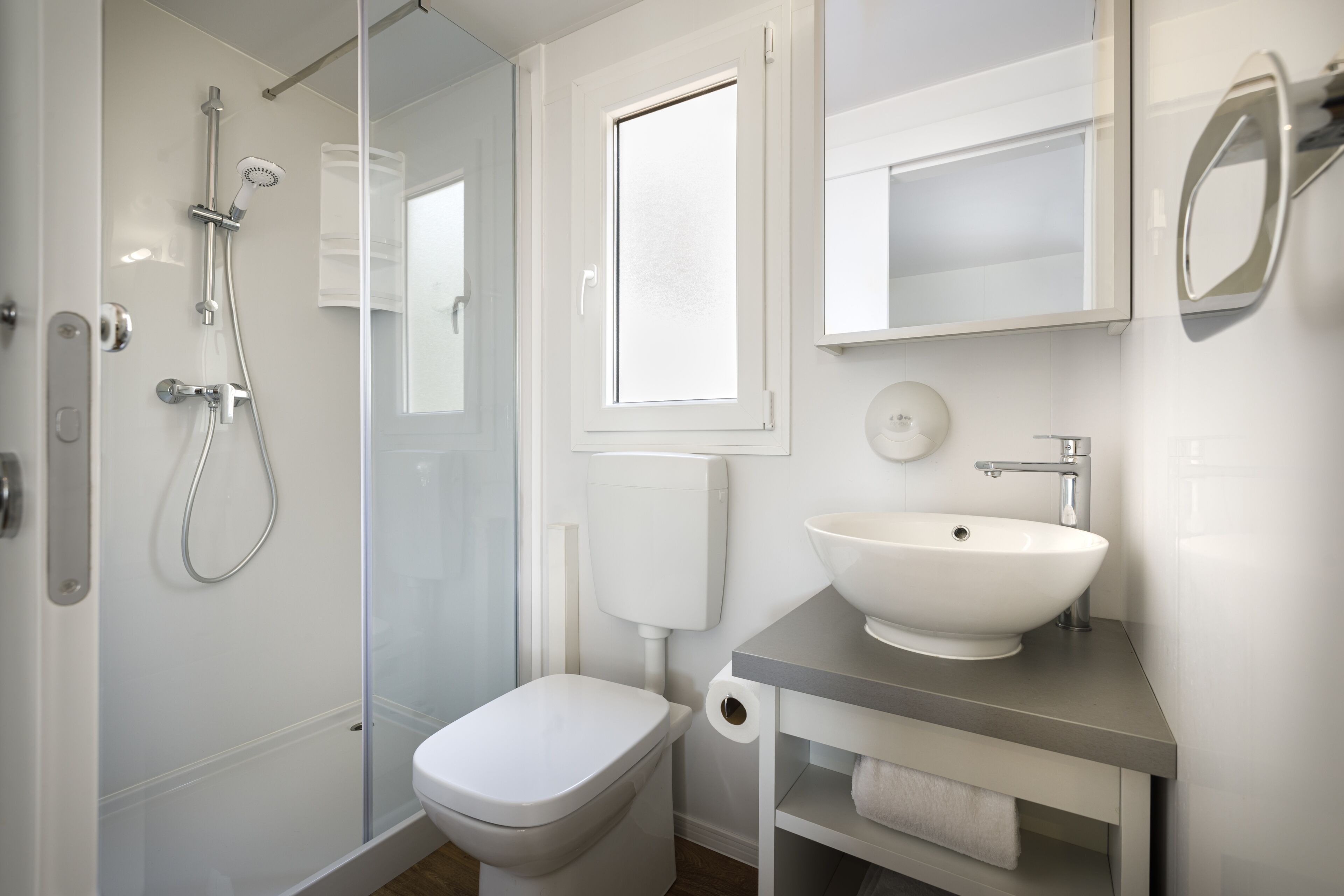 A modern bathroom with a glass-enclosed shower, a white toilet, a sink with a mirror, and a window.