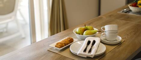 A breakfast table with a bowl of fruit, a plate of pastries, a cup, and a napkin with cutlery.
