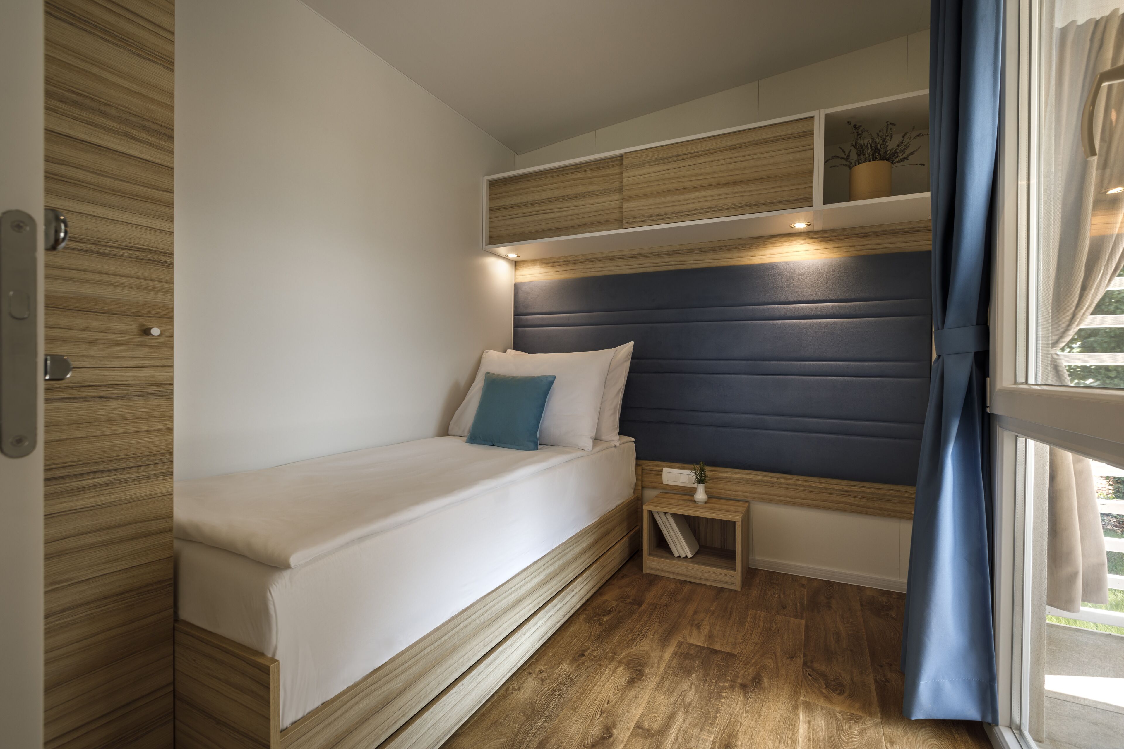 Une chambre à coucher de taille réduite, comprenant un lit, une table de chevet et des étagères intégrées.