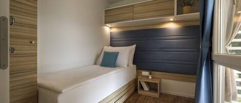 Une chambre à coucher de taille réduite, comprenant un lit, une table de chevet et des étagères intégrées.