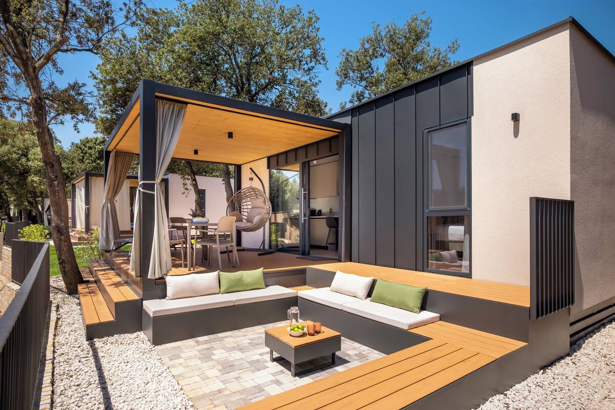 A modern outdoor seating area with a wooden table, cushioned benches, and a pergola.