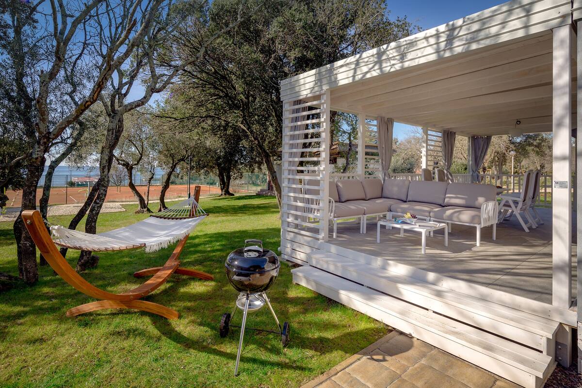 A covered outdoor seating area with a sofa and chairs, a grill, and a hammock.