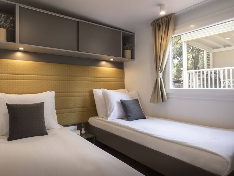 A hotel room with two beds, a built-in shelf with potted plants, a window with curtains, and a view of the outdoors.