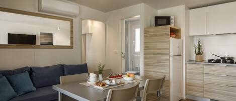 A modern kitchen with white cabinets, a built-in microwave, and a refrigerator. There is a dining table with chairs and a small plant on the counter.